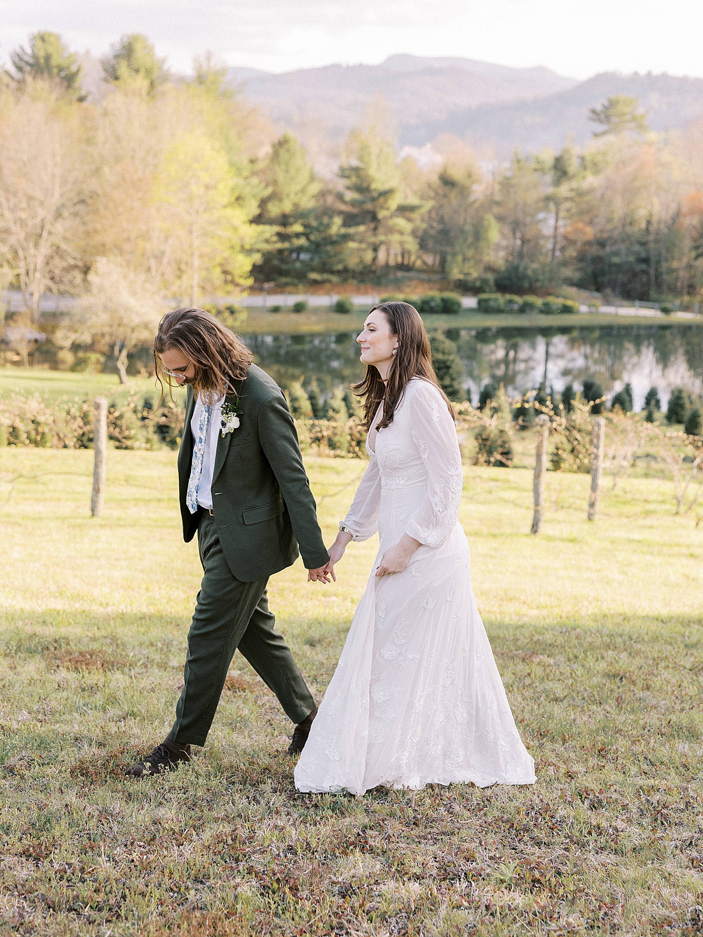 Bride and groom walking hand in hand through a field | Photo by Diane Sotero Photography