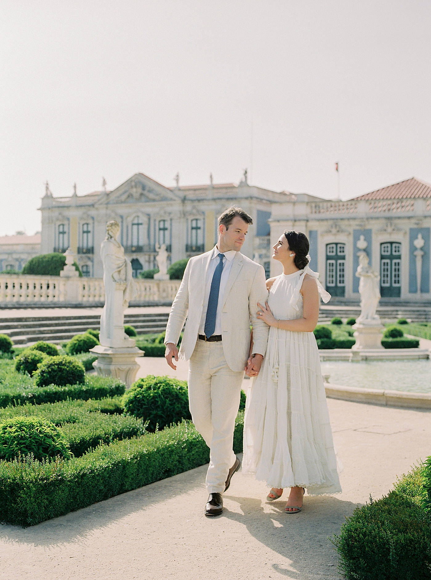 Couple in white and cream attire holding hands at Palacio de Queluz | Photo by Diane Sotero 