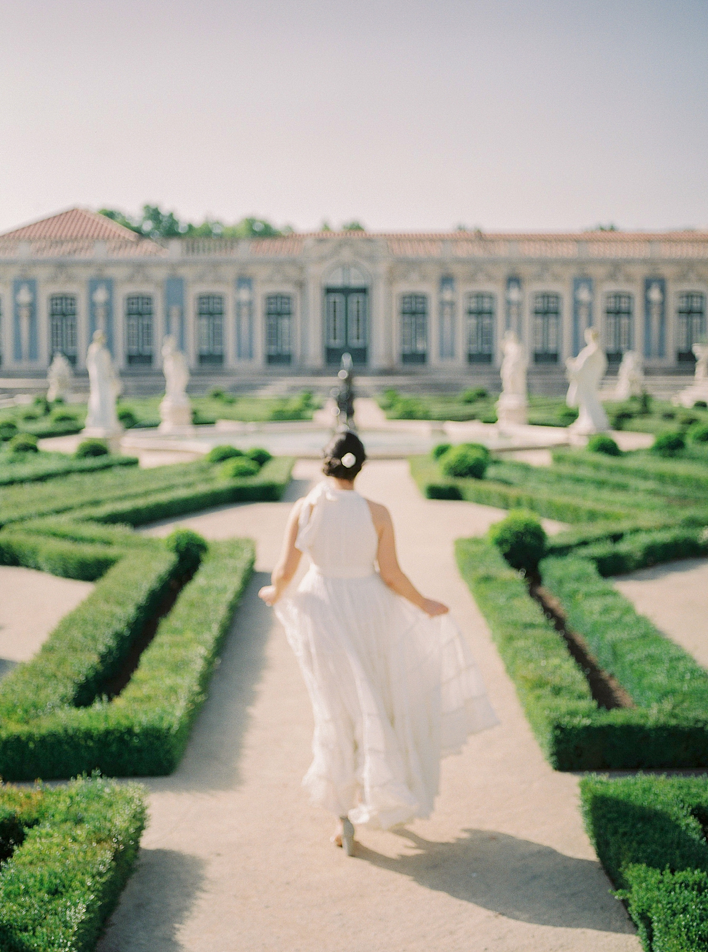 Woman in a white dress running through a garden at Palacio de Queluz | Photo by Diane Sotero 