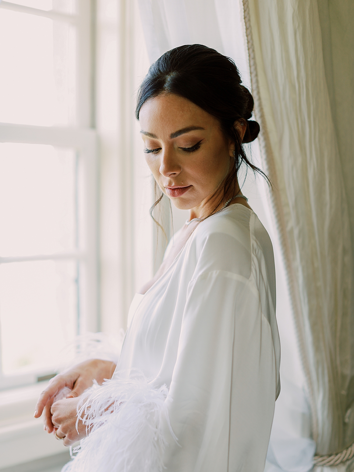 Bride in a robe standing by a window | Image by Diane Sotero Photography