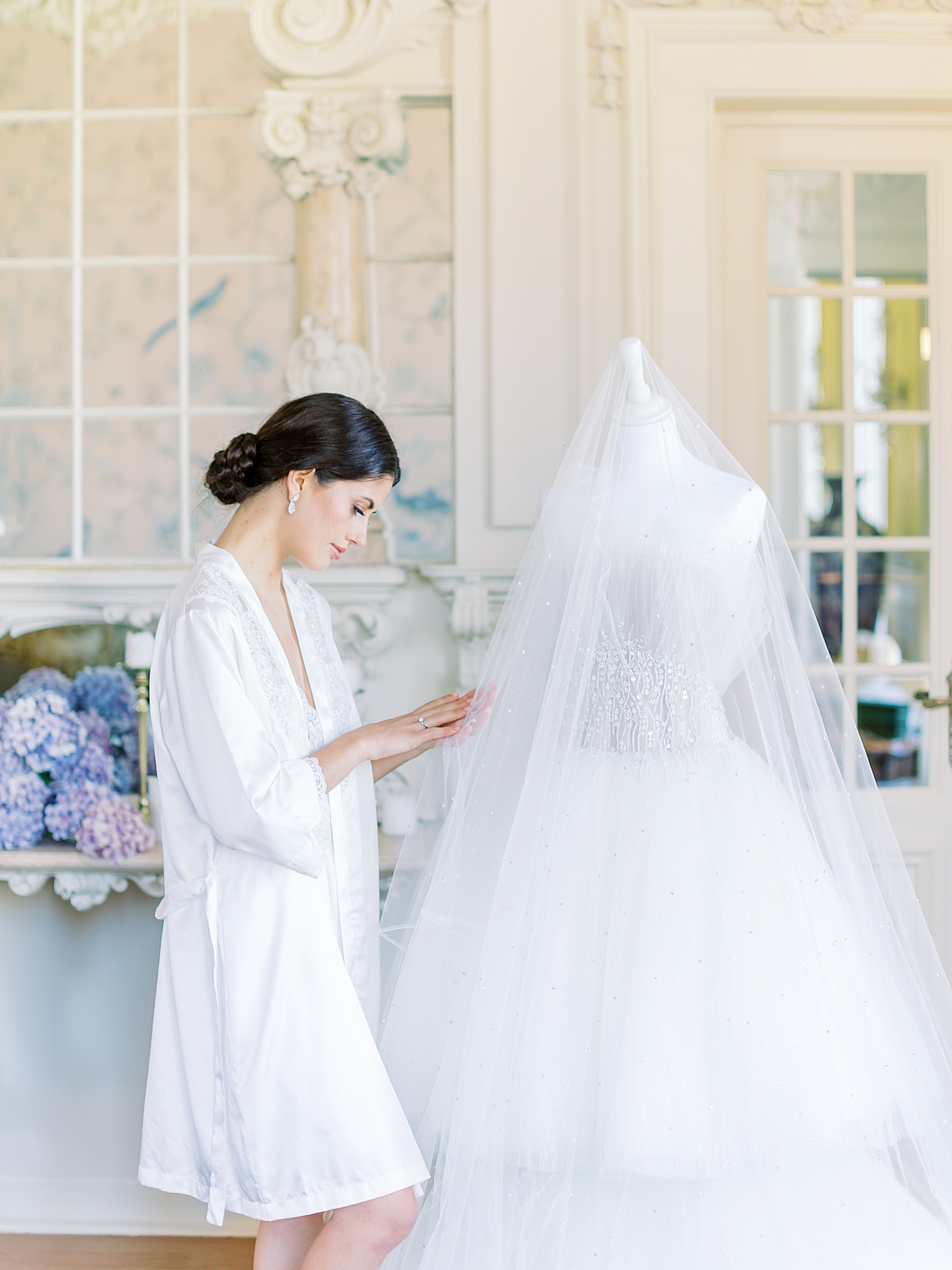 Bride in a white robe admiring her veil | Image by Diane Sotero 