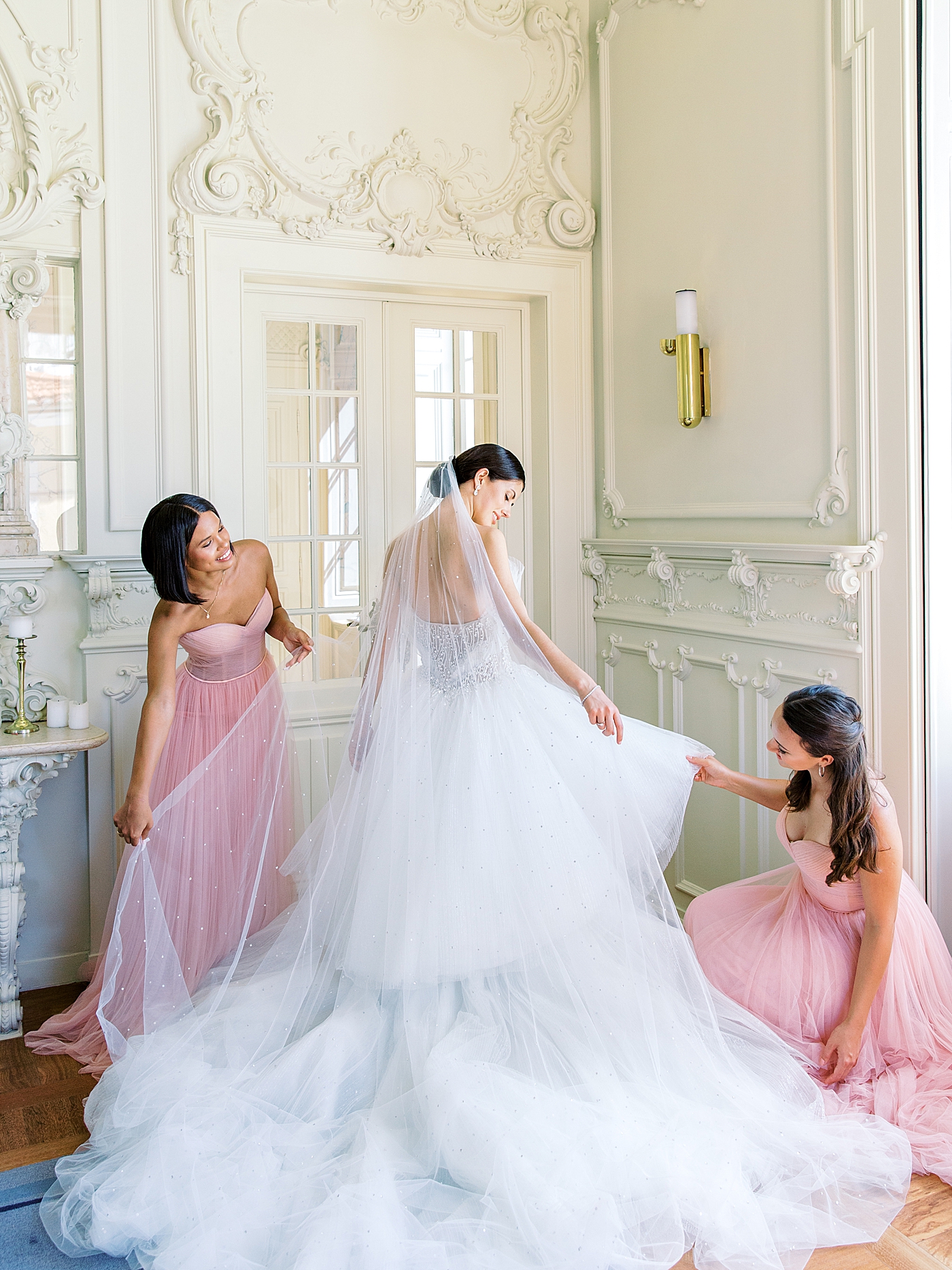 Bridesmaids in pink adjusting brides gown and veil | Image by Diane Sotero 