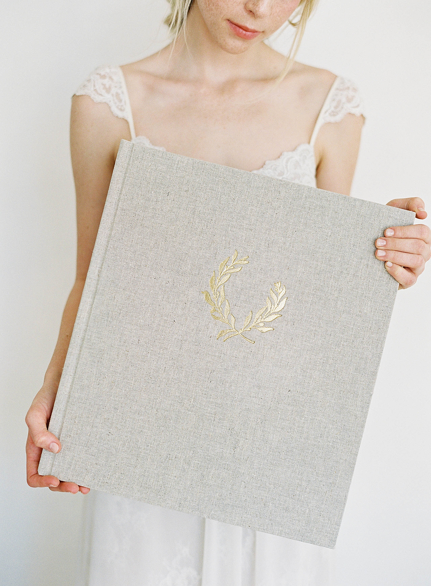 Light gray wedding album with gold details held by woman in white dress | Images Diane Sotero 