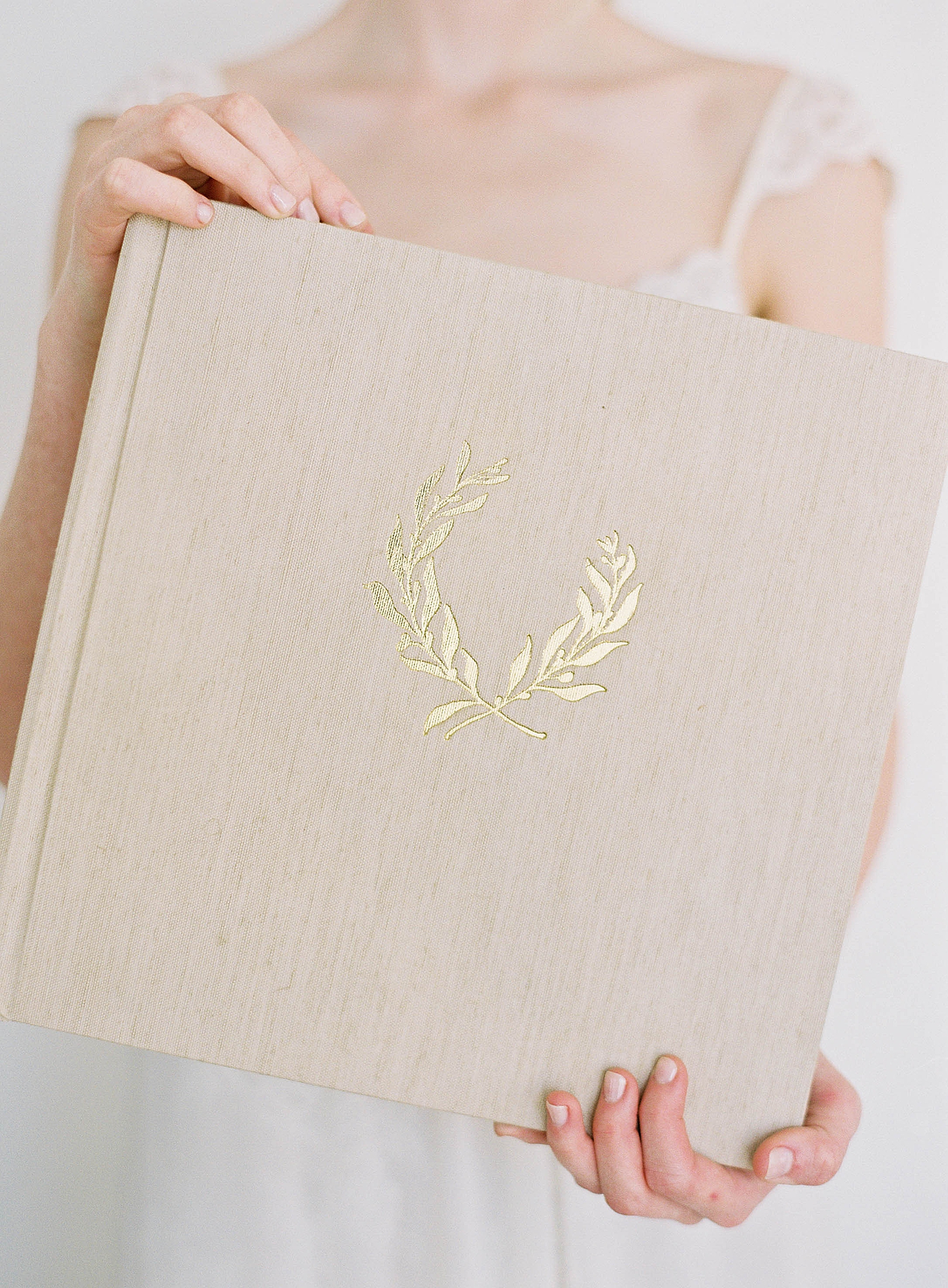 Neutral wedding album with gold detail held by woman in white dress | Fine Art Wedding Albums from Diane Sotero 